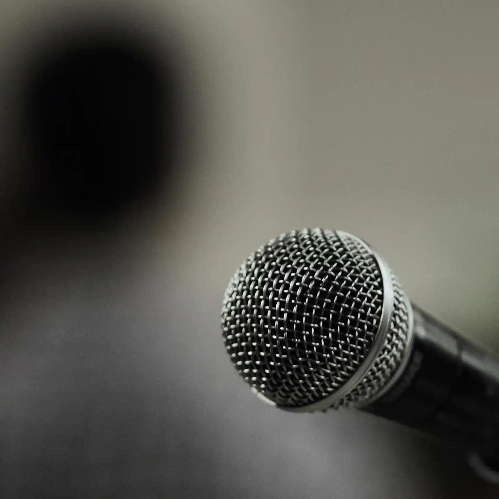 A dramatic, close-up shot focusing on the wire mesh grille of a dynamic microphone against a blurred dark background