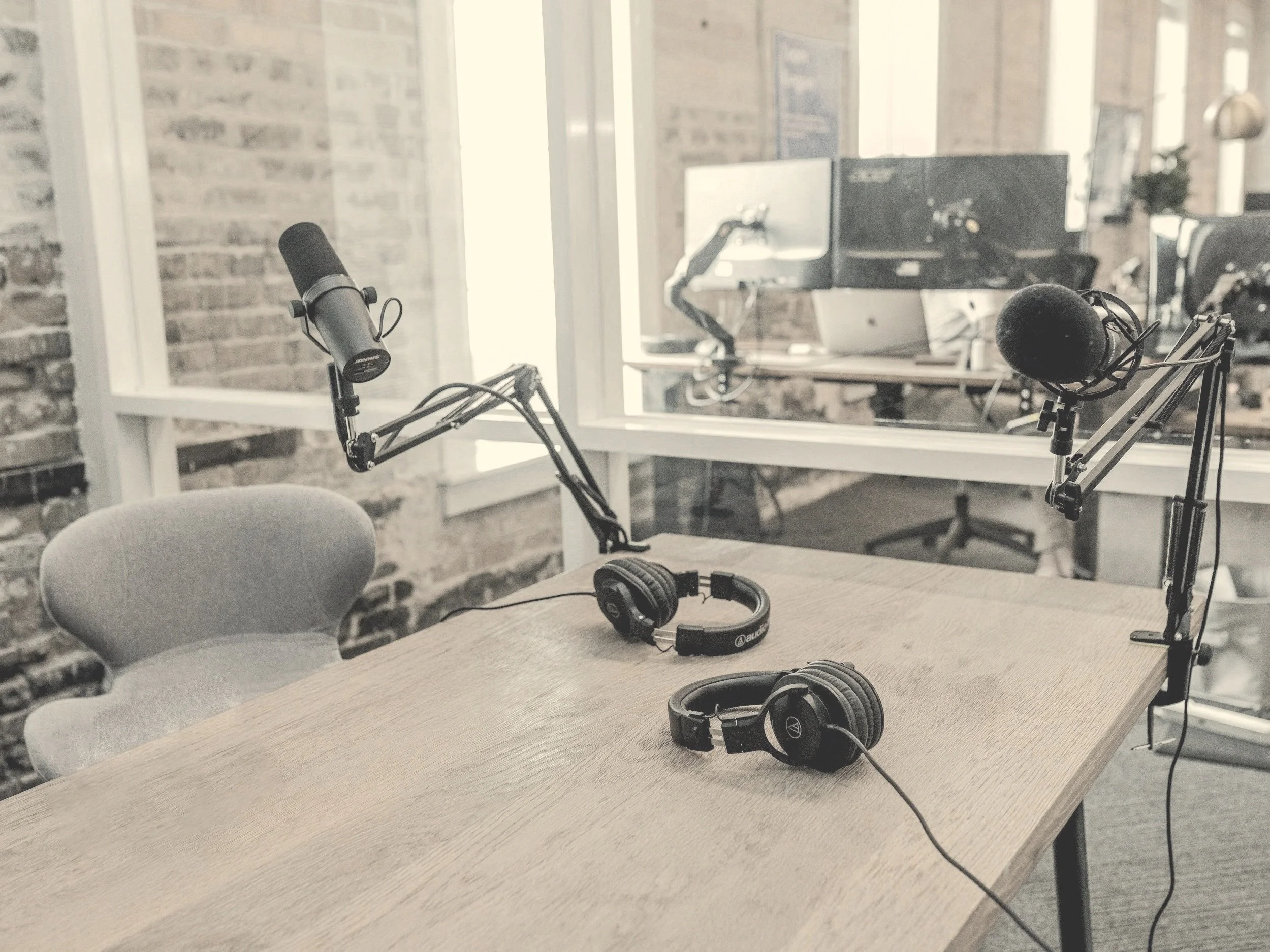 A minimalist podcast studio setup with two microphones on stands, a wooden table, and headphones ready for use
